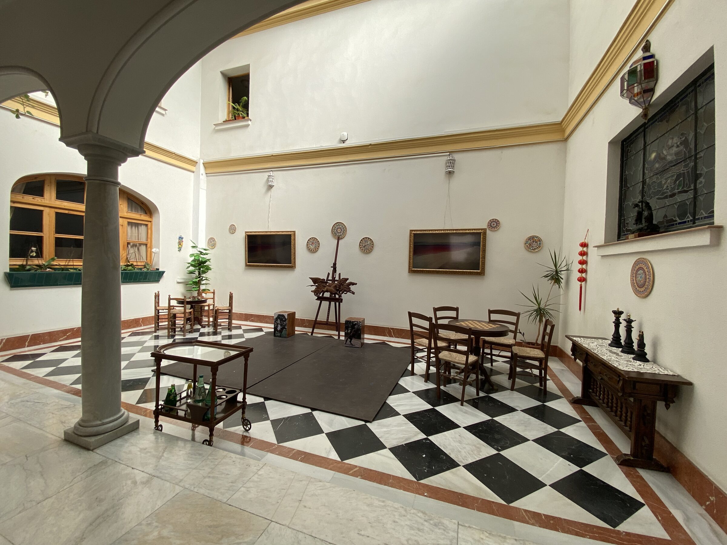 The patio dressed for events — column, painted-yellow trim, ceramic plates, black-and-white checkerboard floor with chess set and easel.